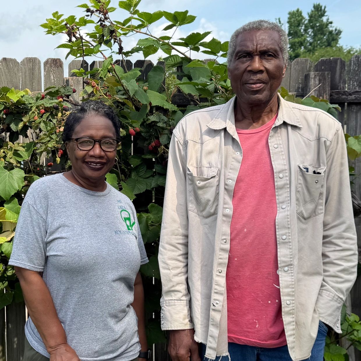 Smiling couple standing in front of a berry-covered fence.