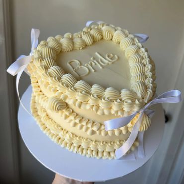 Elegant cream-colored cake with "Bride" written on top and white ribbon accents.