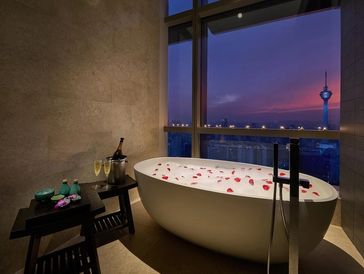 Luxurious bathtub with rose petals overlooking a cityscape at sunset.