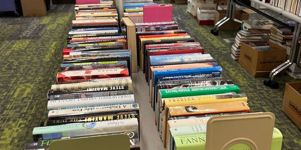 Rows of books displayed on tables at an indoor book sale.