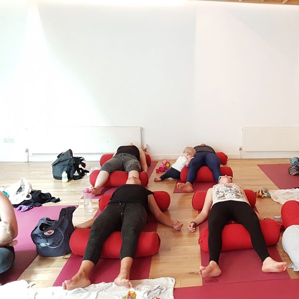 People resting on yoga mats with babies nearby in a calm studio.