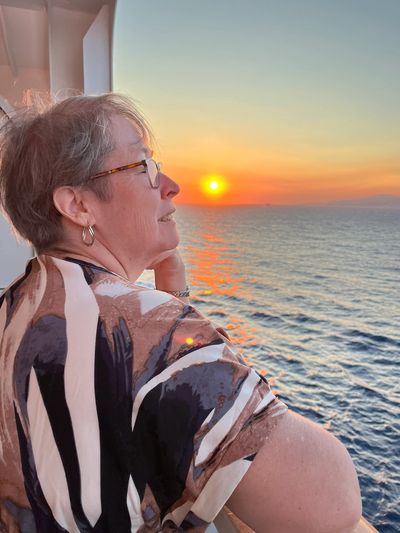 Woman enjoying a serene sunset over the ocean from a balcony.