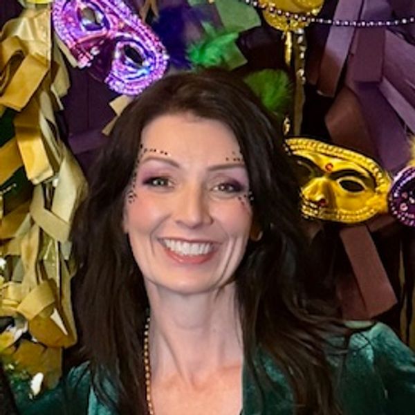 Smiling woman with festive face paint and Mardi Gras masks in the background.