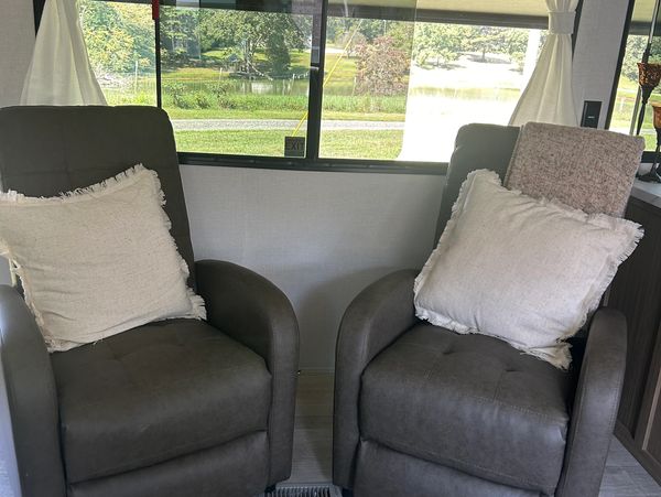 Two gray recliners with white pillows inside a vehicle or trailer.