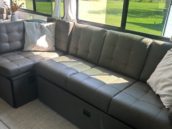 Modern dark gray sectional sofa with pillows by a sunny window.