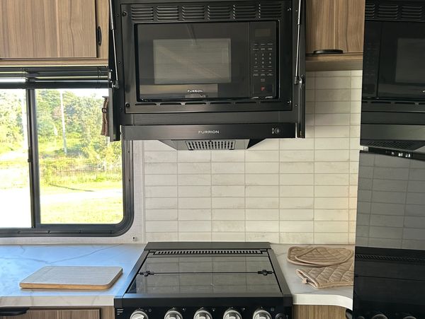 Clean kitchen stovetop with microwave and window.