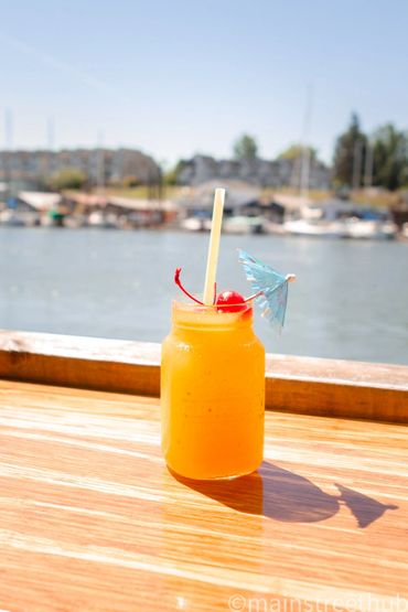 yellow drink with cherry and umbrella on wooden table overlooking the water