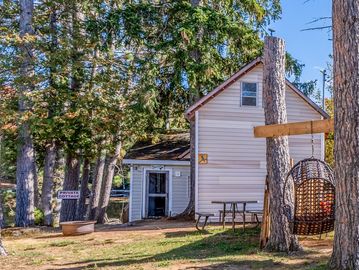 Cozy white cabin near trees and a hanging basket swing.