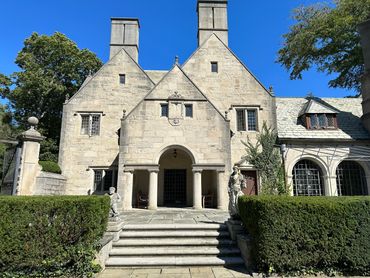 Historic stone mansion with ornate statues and manicured hedges.