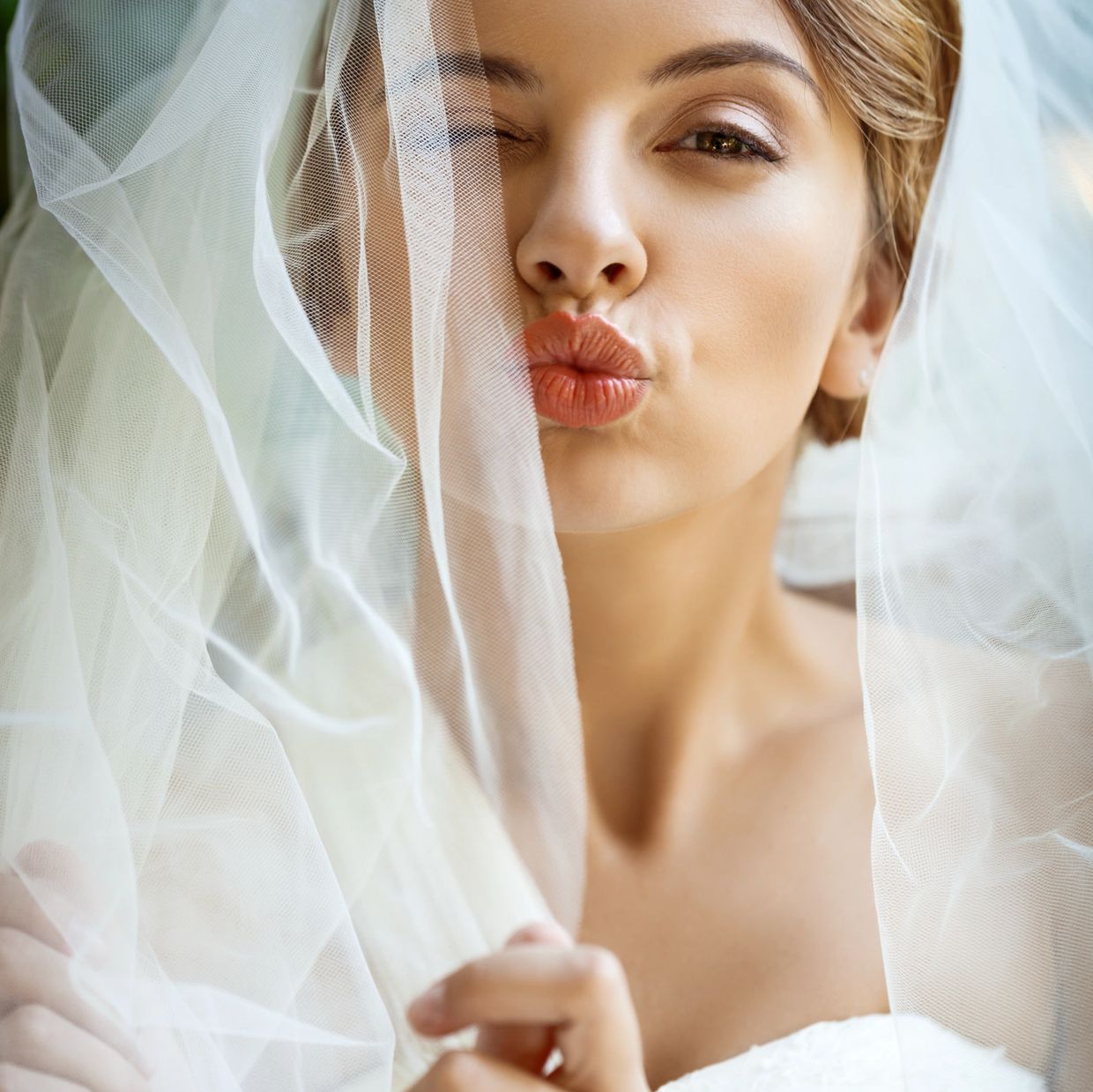 Bride on her wedding day, one eye closed, kissing at the camera