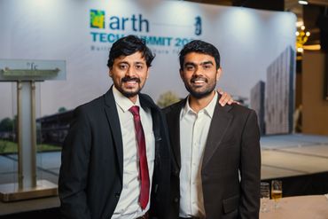 Two men in suits smiling at a tech summit event.