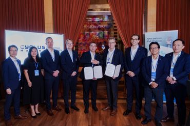 Group of professionals in formal attire posing with signed documents at a business event.