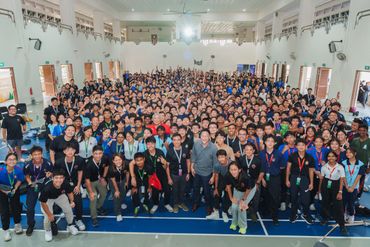 Large group of diverse students and adults posing in a spacious indoor hall.