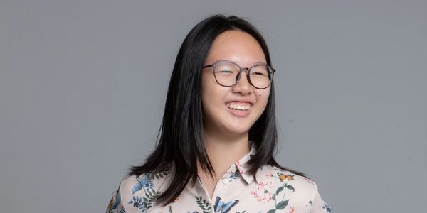 Young woman with glasses smiling against a gray background.