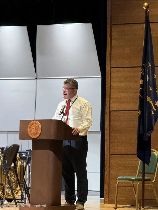 Man speaking at a podium on a stage beside a flag.