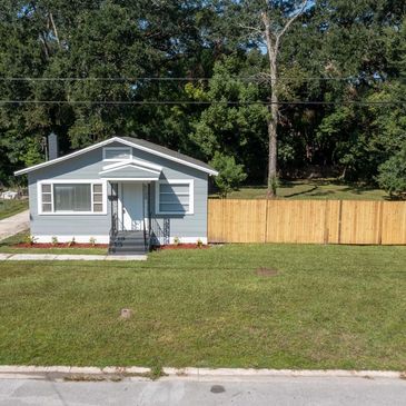 Small blue house with a wooden fence and green lawn.