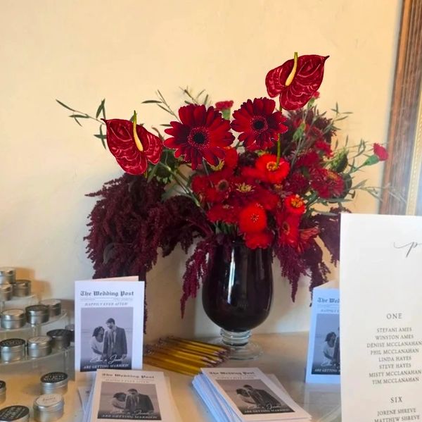 Vibrant red flower arrangement on a table with wedding booklets and candles.