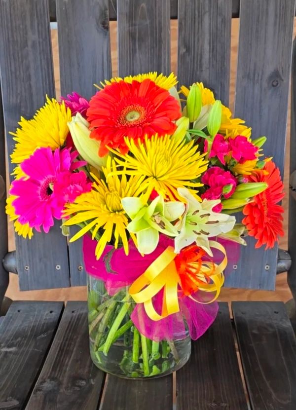 Colorful flower bouquet in a glass jar with a pink and yellow ribbon.