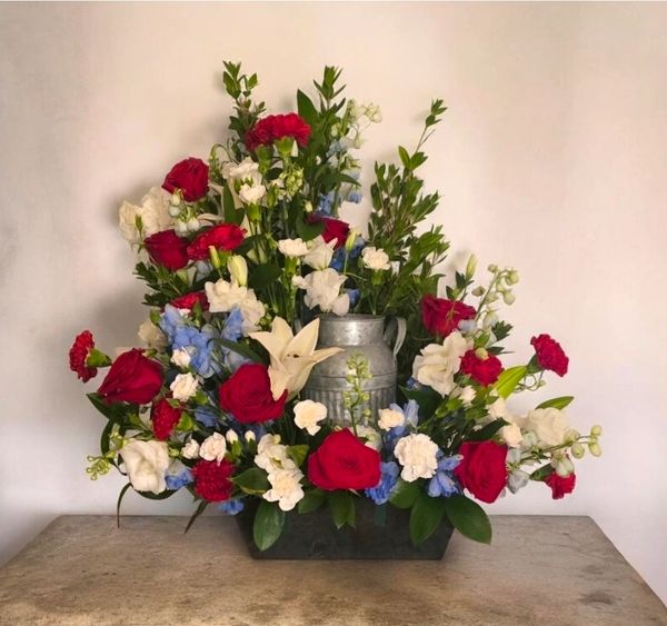 Vibrant floral arrangement with red, white, and blue flowers in a metal vase.