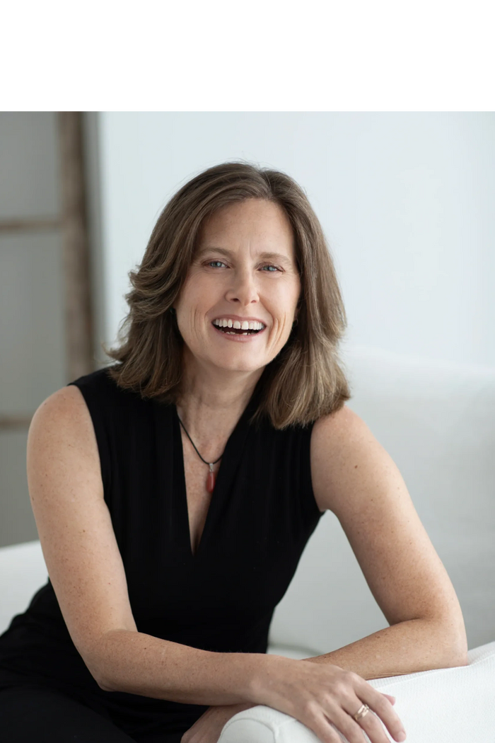 Smiling woman in a black sleeveless top sitting on a white couch.