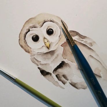Watercolor painting of an owl with paintbrushes.