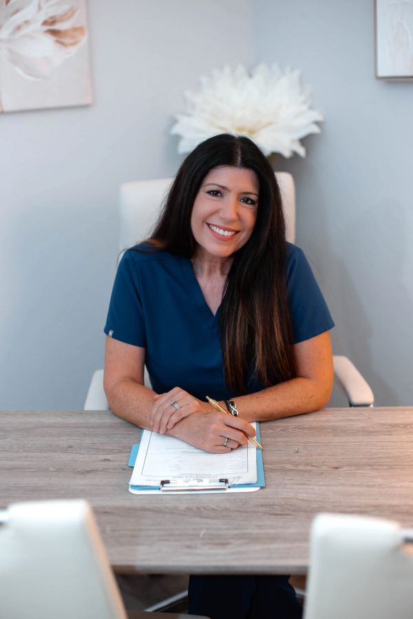 Smiling woman in navy scrubs at a desk with clipboard.