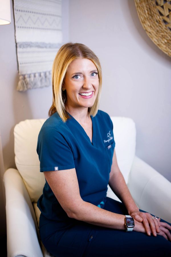 Smiling woman in blue scrubs sitting on a white chair.