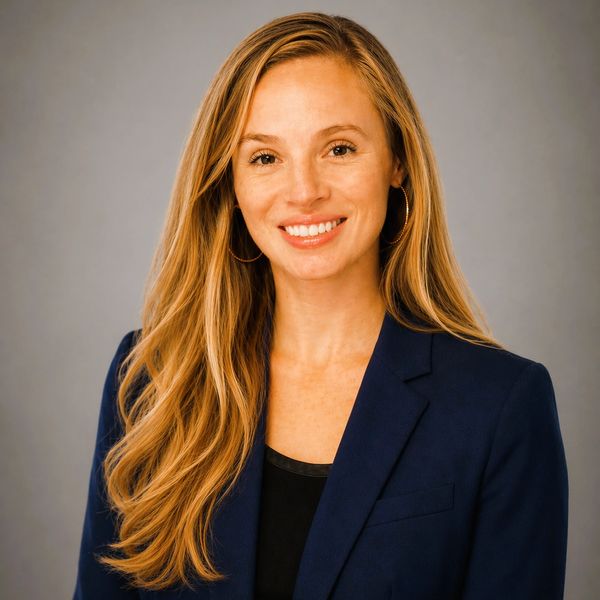 Smiling woman with long blonde hair in a navy blazer against a gray background.