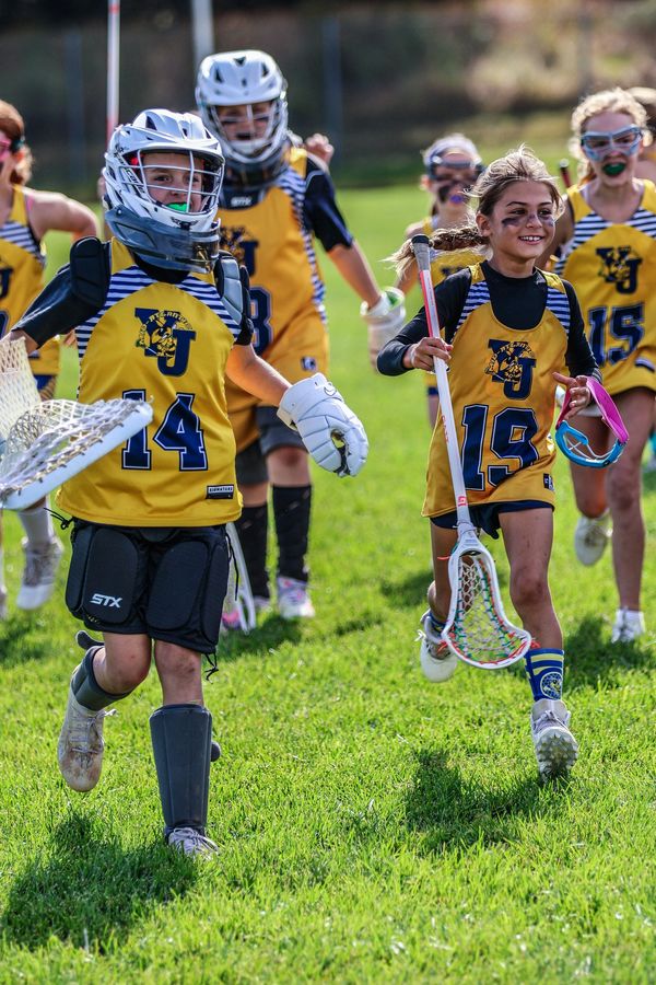 Young lacrosse players running on field in yellow jerseys.