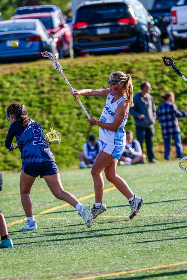 Girls playing lacrosse on a sunny day.