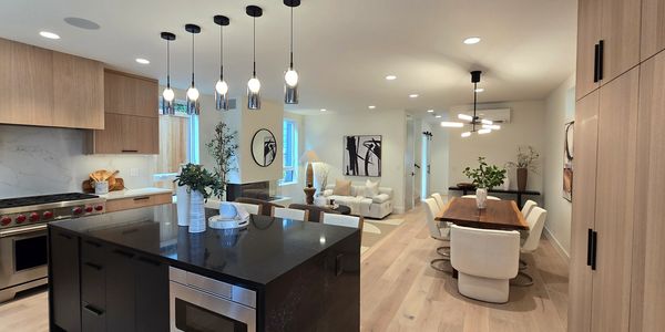 Open-concept kitchen with wood cabinets, quartz island, pendant lighting, and stainless appliances.