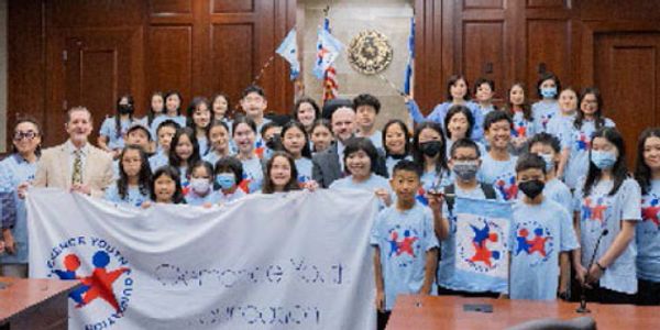 Group photo of children and adults in matching shirts holding a banner indoors.