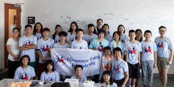 Group photo of diverse youth and adults wearing matching shirts holding a Clemence Youth Foundation banner.