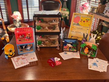 A table displays various Pokémon-themed dioramas, cards, and decorations.