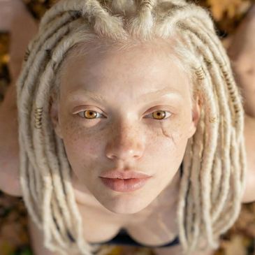 Close-up of a person with blonde dreadlocks and amber eyes looking up.
