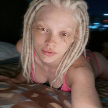 Person with white dreadlocks and unique eye makeup lying down.