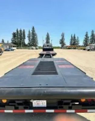 Flatbed trailer parked on a dirt lot under a clear sky.