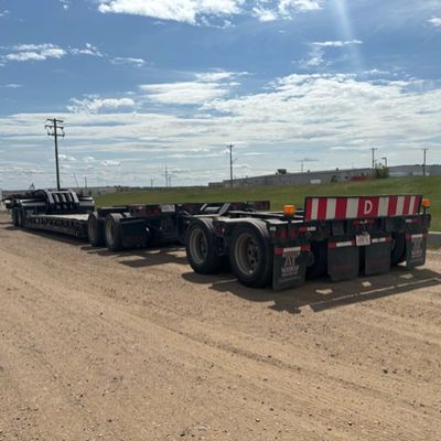 A large flatbed trailer parked on a dirt road under a partly cloudy sky.