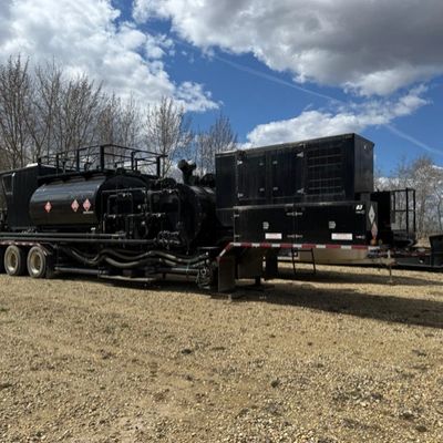 Large black industrial equipment parked outdoors under a partly cloudy sky.