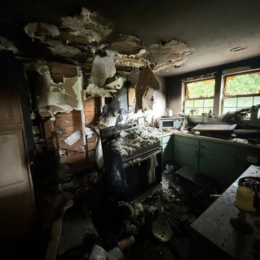A kitchen severely damaged by fire with charred walls and ceiling.