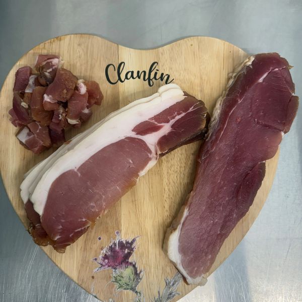 Sliced and diced cured meat on a heart-shaped wooden board.