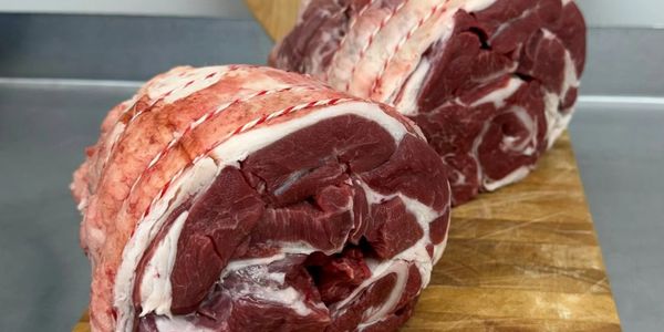 Two rolled cuts of raw meat on a wooden board.