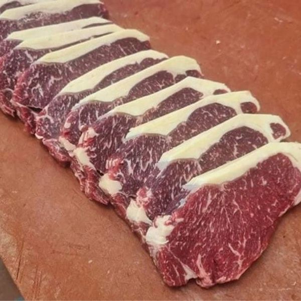 A row of marbled raw steaks neatly arranged on a wooden surface.