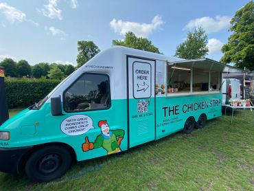 Food truck named The Chicken Stop serving customers at a park.