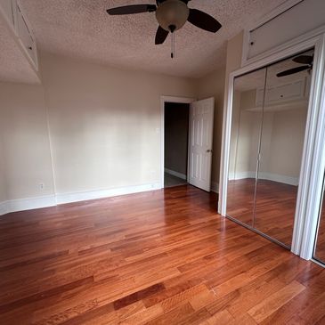 Empty room with wooden floor, mirrored closet doors, and ceiling fan.