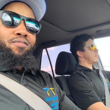 Two men wearing sunglasses and black shirts inside a car.