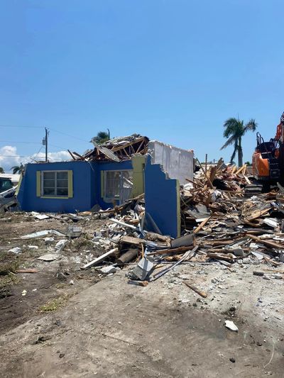 Demolished blue house reduced to rubble under clear skies.