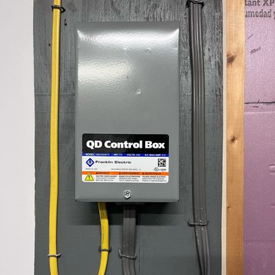 A gray QD Control Box for a 3-wire Pump with yellow and gray power cables mounted on the wall.