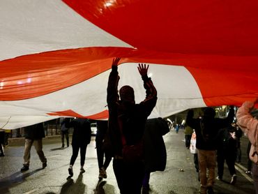 People holding up a large red and white flag during a nighttime gathering.