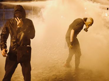 Two individuals in protective gear amidst thick smoke or tear gas.